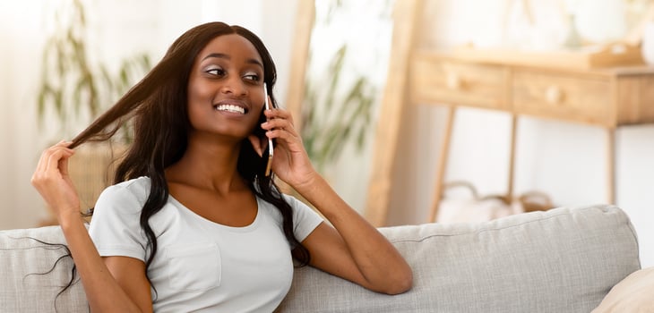 Portrait of gorgeous black woman speaking on mobile phone and smiling while relaxing on sofa at home. Cheerful African American lady discussing news with her family or friends on cellphone photo