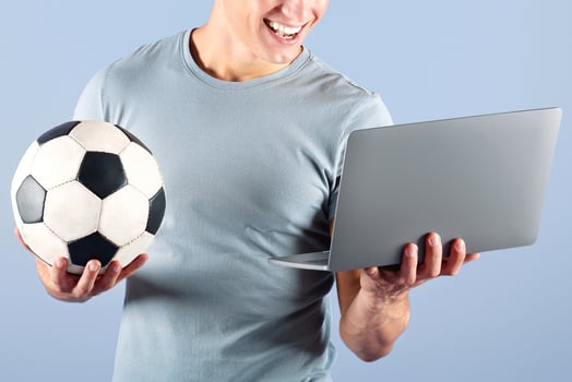 Happy football fan watching online soccer championship on laptop computer over lilac studio background. Handsome young guy cheering for his favorite sports team on internet photo
