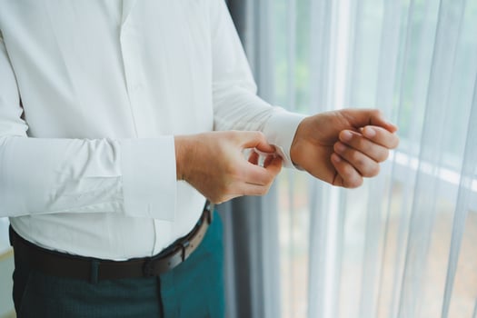 A man adjusting his shirt cuffs by a bright window, showcasing professionalism and style photo