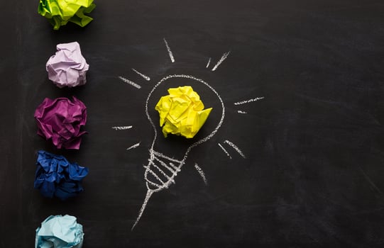 Creative inspirational background - light bulb as metaphor for idea. Electric bulb drawn on chalkboard with yellow crumpled paper for glow. Innovation and barainstorming concept, top view, copy space photo