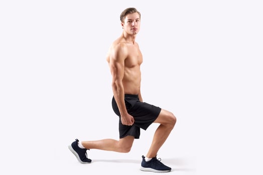 Strong young guy with sexy muscular body doing lunges, warming up before workout over light studio background. Full length portait of handsome shirtless man exercising, stretching legs photo