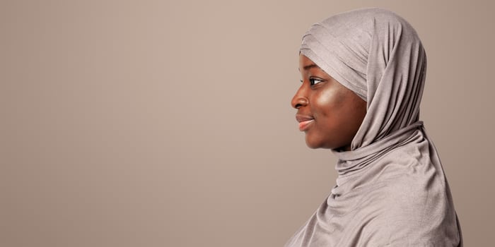 Profile portrait of black islamic lady in hijab looking at copy space over light background in studio, side view shot of friendly smiling african muslim woman in headscarf, panorama photo