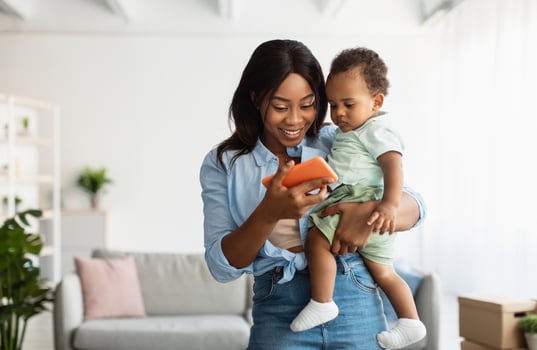 Happy young African American woman showing funny educational application on mobile phone to cute small son, lady holding baby on hands relaxing together, female using digital gadget, watching videos photo