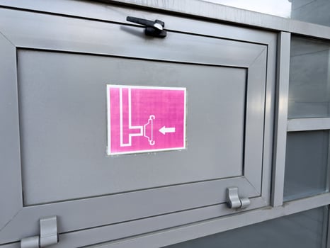 Close up of gray metal cabinet with pink fire hose reel sign showing schematic icon and directional arrow, part of exterior fire safety system installed on public or commercial building facade photo