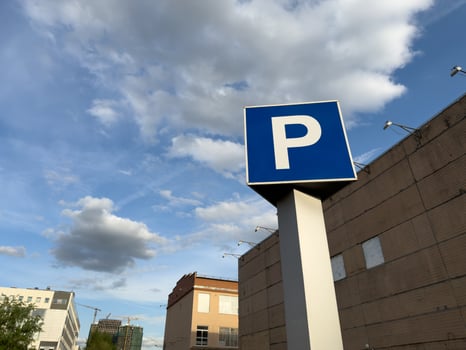 Large, bold blue P parking sign stands tall in the foreground of an industrial style urban building, framed by dramatic sky and scattered clouds, highlighting the practical side of city architecture photo