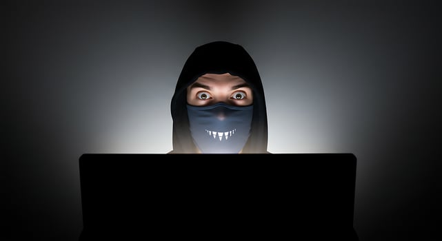 Person Using Laptop Wearing Mask and Hood in Dark Room photo