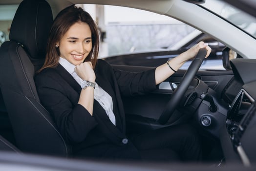 Businesswoman smiling and holding steering wheel while sitting in new car at dealership photo