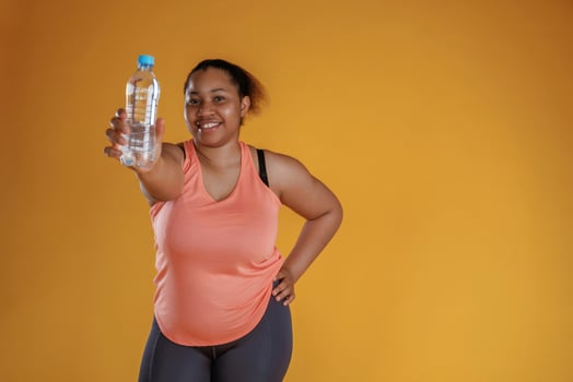 Showing ,bottle of, water. African American woman is in the studio against yellow background photo
