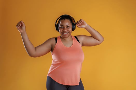 Front view, in ,headphones, listening to music. African American woman is in the studio against yellow background photo