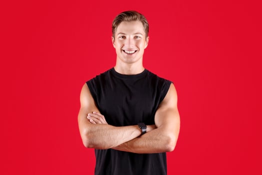 Full length portrait of handsome male fitness model with crossed arms looking at camera on red studio background. Professional young athlete in sportswear posing and smiling photo