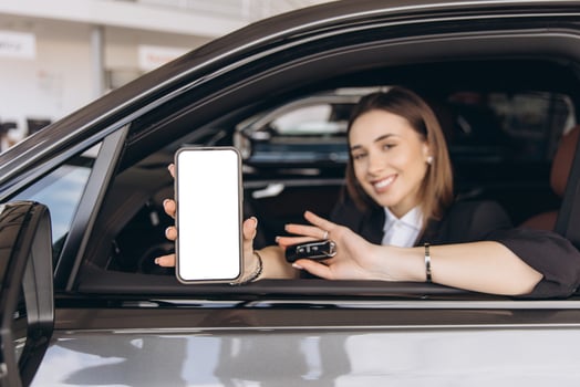 Saleswoman showing smartphone and car key inside new vehicle photo