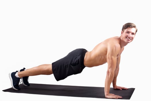 Smiling millennial sportsman standing in plank pose or doing push ups over light studio background, blank space. Happy young athlete with sexy body exercising on yoga mat, panorama photo
