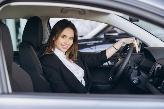 Saleswoman smiling and holding steering wheel of new car in dealership photo