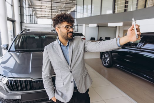 Elegant businessman taking selfie with new car in dealership photo