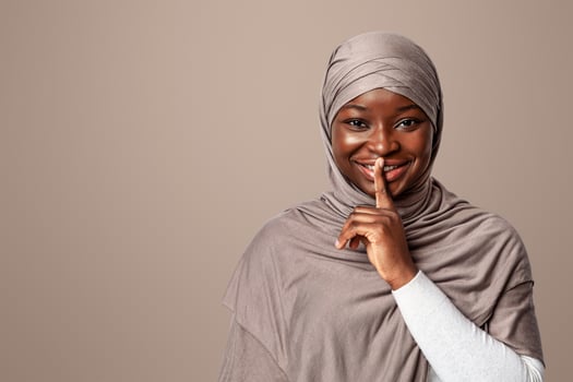 Mysterious Black Muslim Woman In Hijab Showing Shh Sign, Putting Finger On Lips, Smiling African Religious Lady In Headscarf Gesturing Hush And Keep Silence Over Light Studio Background, Free Space photo