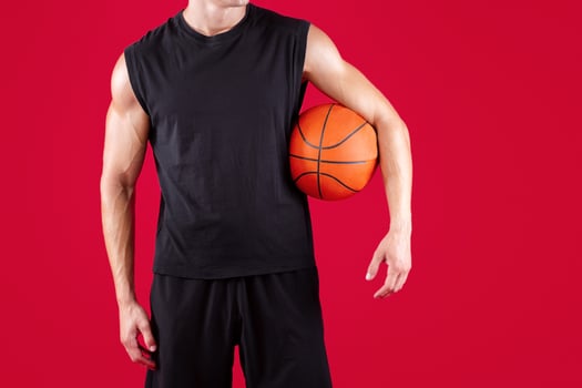 Cropped view of young basketball player holding ball on red studio background, copy space. Millennial athlete in sportswear ready for streetball tournament, close up of hands photo