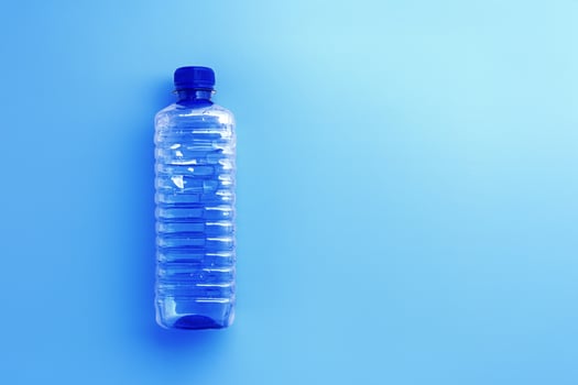 Clear plastic water bottle with blue cap on light blue background with soft shadow, copyspace. Minimal top view photo, themes of ecology, recycling, sustainable living, reduce disposable plastics photo