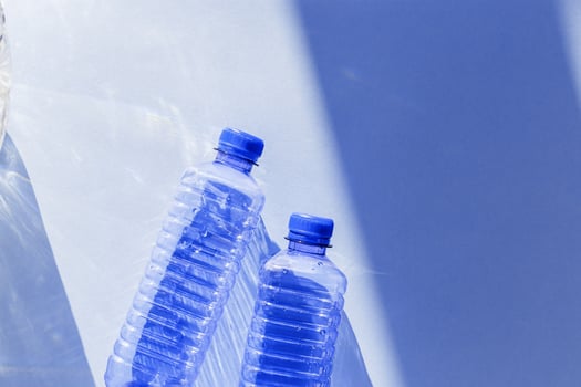plastic bottles with blue caps and sun shadows on light background. Top view Water bottles at natural light. Themes of recycling, sustainability, water conservation, minimal style photo