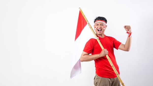 Excited Indonesian man celebrate Indonesia independence day on August 17 by holding the Indonesian flag and raising hand fist in the air isolated on white background photo