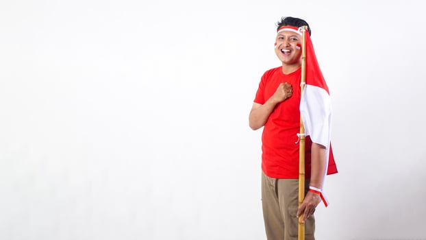 Portrait of Happy Indonesian man celebrate Indonesia independence day on August 17 by holding the Indonesian flag and put his clenched hand in front of his chest isolated on white background photo