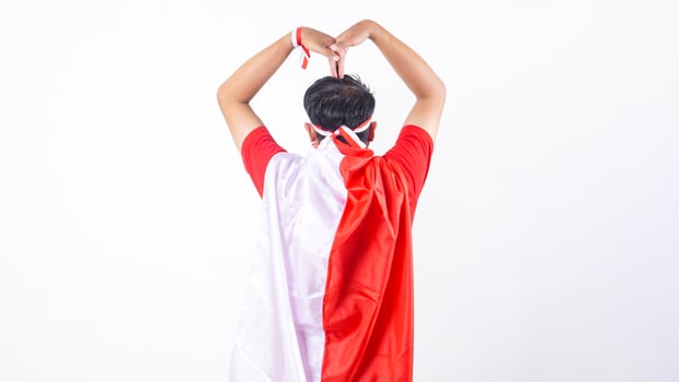 Rear view of Indonesian man celebrate Indonesia independence day on August 17 by tied the Indonesian flag behind his back and doing heart pose isolated on white background photo