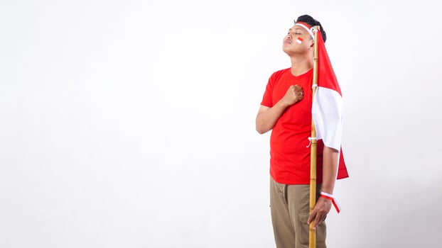 Indonesian man celebrate Indonesia independence day on August 17 by holding the Indonesian flag and put his clenched hand in front of his chest solemnly isolated on white background photo