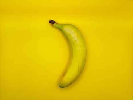 One bright yellow banana on a yellow background in the center of the image, top view photo