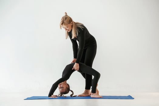 Woman is,, helping girl. Mother and little daughter are in fitness clothes on yoga mat photo