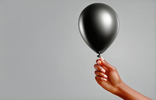 Black Balloon Held by a Hand Against a Light Gray Background in a Minimalist Setting photo