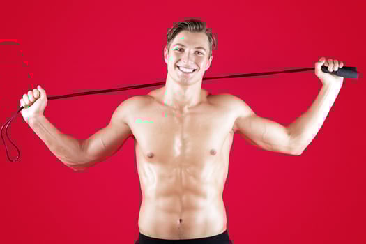 Smiling millennial guy with muscular body holding jumping rope on red studio background. Portrait of sexy sportsman with six pack abs doing cardio or aerobic exercises, promoting healthy lifestyle photo