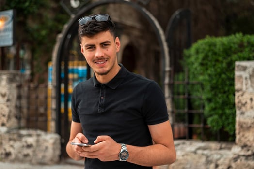 A young happy man using a phone mobile in the city street, looking at a camera and smiling. photo