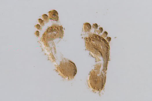 Fresh footprints are visible in fine sand, suggesting someone has recently walked along the shoreline. The light reflects off the sand, creating a peaceful beach atmosphere. photo