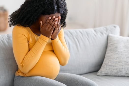 Hormonal changes during pregnancy. Young pregnant african american woman feeling sad and crying at home, sitting on couch at living room alone, feeling lonely and depressed, free space photo