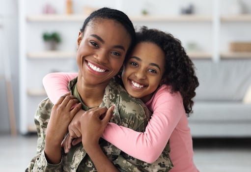 Portrait of cheerful pretty curly black teen girl hugging her mom soldier from behind and smiling at camera, young black woman in military uniform return home from army, cuddling with her daughter photo