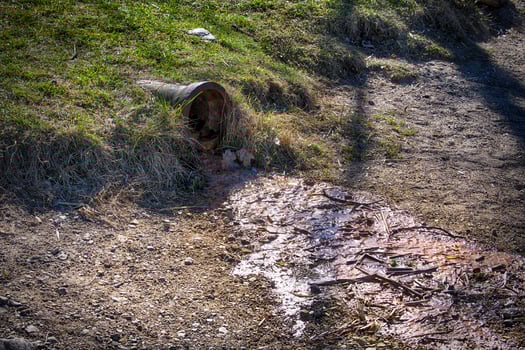 Polluted Water Flowing From a Rusty Drain Pipe Into Contaminated Soil in a Rural Outdoor Environment photo