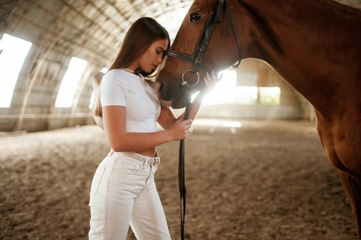 Side view, ,embracing the animal. Beautiful young woman is with horse indoors photo