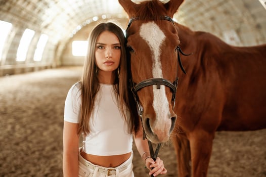 In white clothes, standing. Beautiful young woman is with horse indoors photo