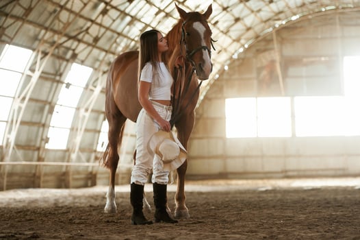 Daylight comes through ,the windows. Beautiful young woman is with horse indoors photo