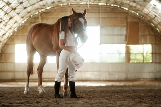 Holding, cowboy hat in ,hand. Beautiful, young woman is with horse indoors photo