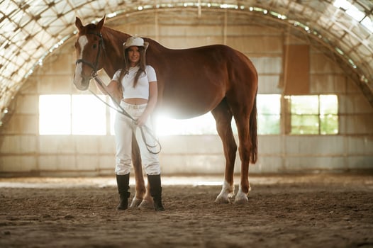 Standing and posing. Beautiful ,young woman is with horse indoors photo