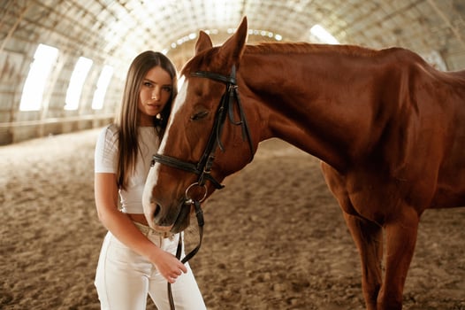 In, white clothes, standing. Beautiful young woman is with horse indoors photo