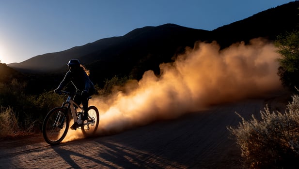Silhouette of cyclist kicking up dust on mountain trail at dawn photo