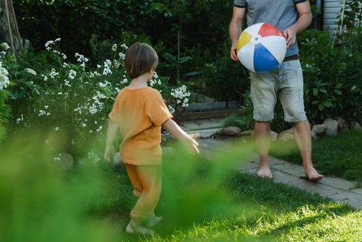 Summer family time, outdoor leisure activity. Dad and small son playing with inflatable ball on lawn in backyard . photo