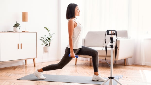 Online Workout Concept. Active asian lady filming home training tutorial on camera, doing lunges with dumbbells, exercising on yoga mat. Trainer recording for internet channel in living room photo