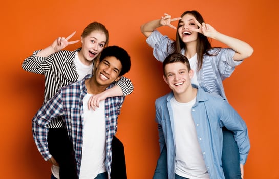 Happy friends having fun. Guys giving piggyback ride to girls, fooling over orange background photo