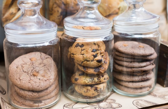 Desserts choice. Cookies and biscuits in glass jars on counter bar for sale. Chocolate drops and chips, oatmeal cookies stacks. photo