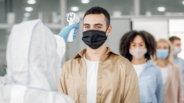 Checking temperature morning before work. Man in hazmat suit control first symptoms of illness at workers in protective masks in office, during covid-19 epidemic, empty space, close up photo