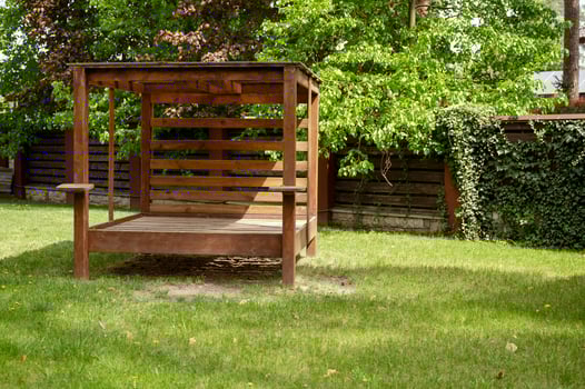 Wooden brown gazebo with a canopy in the middle of the garden. Picnic gazebo among green trees, surrounded by a fence with ivy, on a bright lawn. photo