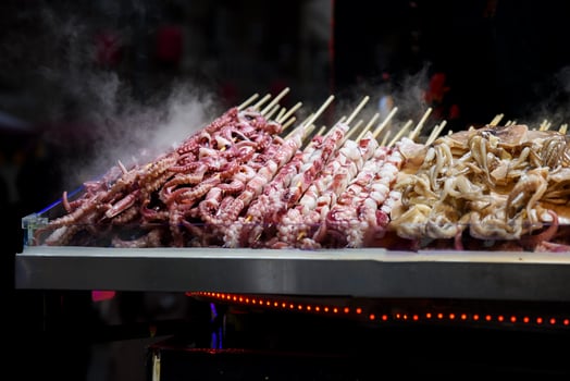 Night street food market in Shanghai, China. Grilled seafood skewers octopus and tentacles sizzling on fire. Dark, atmospheric vibe. photo