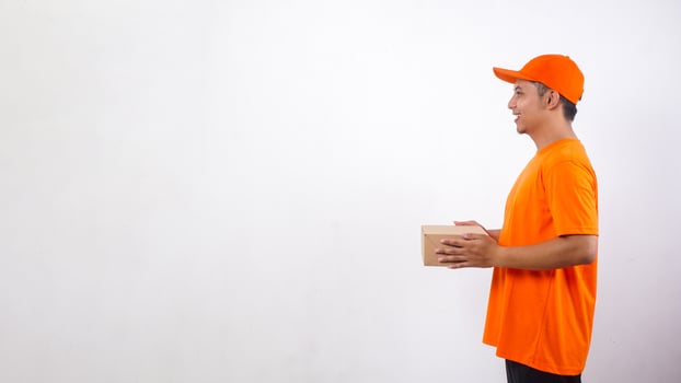 Side view of Asian deliveryman in orange t-shirt uniform holding a package box parcel isolated on white background photo